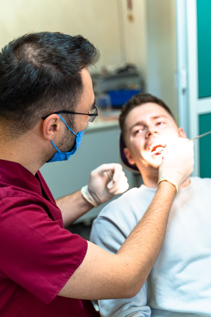 Medicul lucrând la scaunul stomatologic, explicând pacientului.